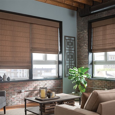 The corner of a modern-industrial Kansas City home living space, featuring matching roller shades emulating a natural texture. By The Blind Broker.
