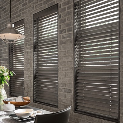 Dark, natural-tone wooden blinds against complimentary stone-finish interior walls of a Kansas City home's dining area. Available at The Blind Broker.