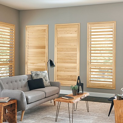 Light-finish wooden shutters in a home living space interior, adding light control and visual contrast. Available at The Blind Broker.