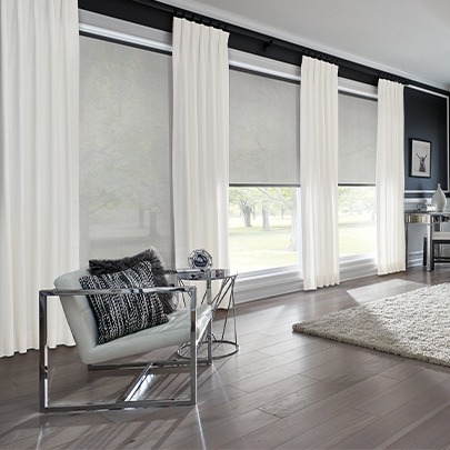 A contemporary Kansas City home's living space with several floor-to-ceiling windows and color-coordinated fabric roller shades and drapes. By The Blind Broker.