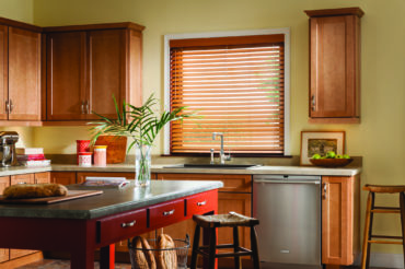 A set of natural, wooden blinds that compliment the surrounding kitchen cabinetry within the featured Kansas City home. By The Blind Broker.