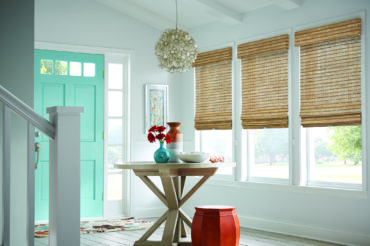 Light-finish wooden woven shades within a Kansas City home's entryway, lending to the ample natural light. Available at The Blind Broker.