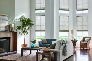 A set of multi-story windows within a Kansas City home's living space, boasting wooden woven shades that allow for some natural light. Available at The Blind Broker.
