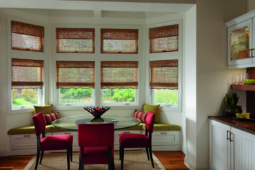 A home's bump-out dining area, featuring two levels of windows with custom wooden woven shades that filter the natural light. Available at The Blind Broker.