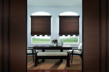 A home dining area, featuring arched windows and wooden woven shades that filter the natural lighting. Available at The Blind Broker of Kansas City.