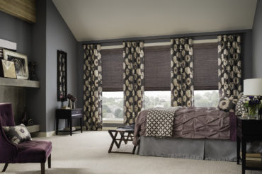 A warm home bedroom featuring natural, jewel tones and wooden woven shades accented by floral drapery. Available at The Blind Broker of Kansas City.