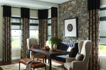Artisan drapes with floral pattern in a dark, inviting dining area with stone accent wall. Styles available at The Blind Broker of Kansas City.