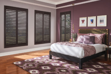 Dark wooden shutters in a home bedroom, accentuating the romantic atmosphere with mauve and violet tones. Available at The Blind Broker of Kansas City.