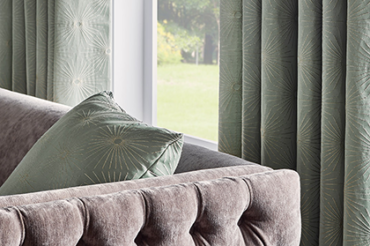 Mid-century drapes and natural-shade roller fabric shades complimenting the interior living space's decor. By The Blind Broker of Kansas City.