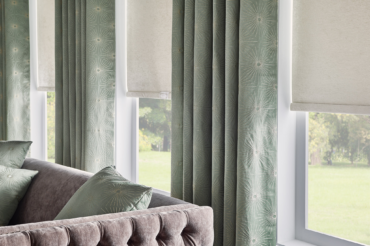Mid-century drapes and natural-shade roller fabric shades complimenting the interior living space's decor. By The Blind Broker of Kansas City.